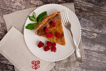 Sweet home-made cheesecake served with raspberries on a white plate on vintage wooden background, flat lay