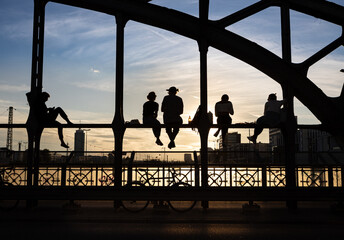 Unrecognizable backlit people enjoying the sunset sitting on a steel bridge construction over...