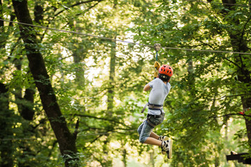 Little boy overcomes the obstacle in the rope park. Climbing in high rope course enjoying the adventure. Adventure climbing high wire forest - people on course in mountain helmet and safety equipment.