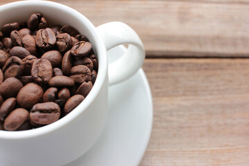 Cup of coffee beans on a wooden table. Close-up of coffee beans in a white ceramic cup on wood background with copy space. Rustic style

