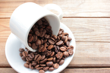 Cup of coffee beans on a wooden table. Close-up of coffee beans in a white ceramic cup on wood background with copy space. Rustic style

