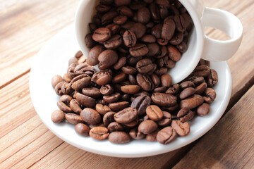 Cup of coffee beans on a wooden table. Close-up of scattered from a white ceramic cup coffee beans on wood background. copy space. Rustic style
