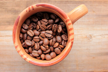 Cup of coffee beans on a wooden table. Close-up of coffee beans in a brown ceramic cup on wood background with copy space. Rustic style
