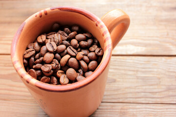 Cup of coffee beans on a wooden table. Close-up of coffee beans in a brown ceramic cup on wood background with copy space. Rustic style
