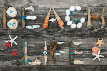 Abstract of driftwood, seashells, pebbles and blue cobalt seaglass forming the word beach life on rustic wood background. 