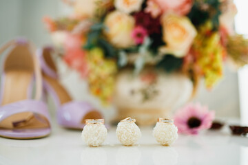 Obraz na płótnie Canvas Wedding rings and an engagement ring on Raffaello candies on a white table with flowers on a blurred background.