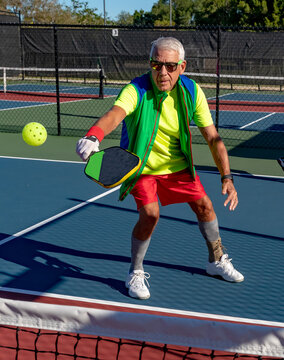 Senior man volleys a pickleball over the net