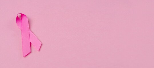 Pink ribbon breast cancer awareness symbol on pink background. Panoramic image with copy space. 