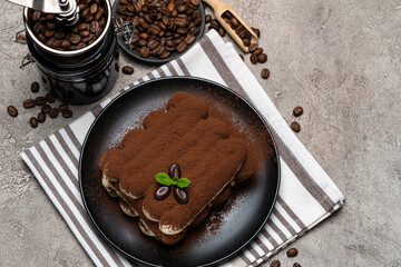 Classic tiramisu dessert and coffee grinder on ceramic plate on concrete background