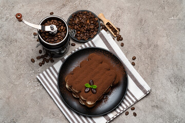 Classic tiramisu dessert and coffee grinder on ceramic plate on concrete background