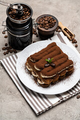 Classic tiramisu dessert and coffee grinder on ceramic plate on concrete background