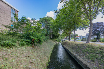 Keutelbeek stream flowing between houses and buildings beside a street with lush trees, sunny summer day with a blue sky in Sittard, South Limburg, Netherlands