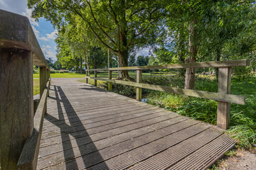 Small wooden footbridge over the Keutelbeek stream with lush green trees on the shore seen from a bottom perspective, sunny summer day in Sittard in South Limburg, Netherlands