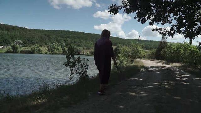 Women in long dress walks along the lake shore. A walk in the fresh air.