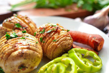 Baked potatoes with carrots. White plate. Wooden background. Delicious and healthy lunch. Hasselback potatoes. Close up