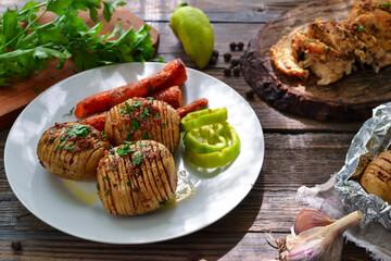 Baked potatoes with carrots. White plate. Wooden background. Delicious and healthy lunch. Hasselback potatoes.