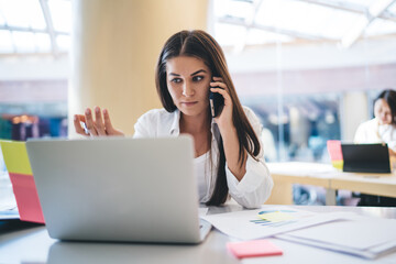Obraz premium Serious female manager making smartphone call for discussing service and project during working process in office, pensive caucasian woman employee calling to support about website development