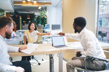 Obraz premium Smiling multiracial crew cooperating on common project in office interior share ideas and documents, positive diverse group of colleagues talking to each other collaborate in friendly atmosphere