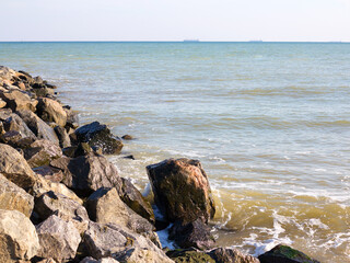 Huge stones of granite on shore of Black sea. Seascape. On horizon in haze of silhouettes of ships and buildings