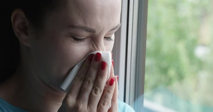 Woman Sneezing into a Napkin Standing by the Window