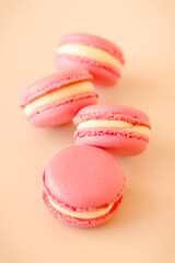 Four pink macaroon cookies with white chocolate cream on beige background