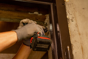 The master drills holes with a hand drill in a metal door box, close-up, installation of new doors.