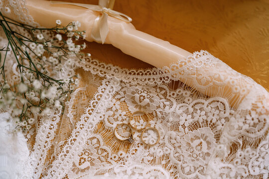 Wedding rings and an engagement ring white wedding dress of the bride with lace and wildflowers on a wooden table.