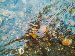 Fototapeta na wymiar Crystal clear water of river surface with small stones and pebbles.