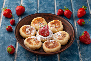 Fototapeta na wymiar Food poster - Cottage cheese pancakes, pancakes, cheesecakes with strawberries in a clay plate on a background of blue wooden boards. Ukrainian and Russian cuisine. Homemade food. Tasty breakfast.