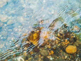 Crystal clear water of river surface with small stones and pebbles.