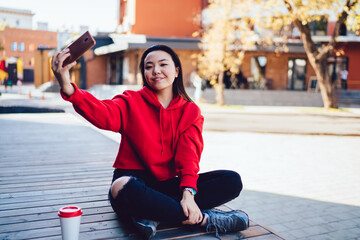 Portrait of carefree millennial user smiling at camera while making media content via smartphone...