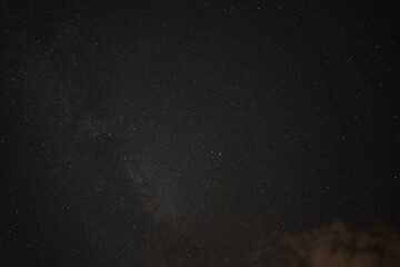 Milky way and many stars in front of a black blue night sky, orange colored cloud in the foreground. Germany.