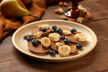 Pancakes with fruits and nuts on dark wood table, closeup