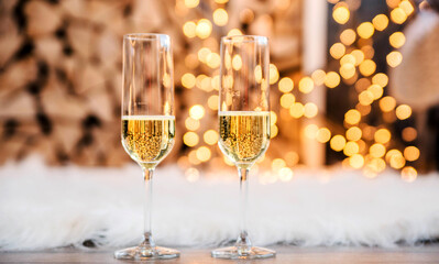 Beautiful two glasses of champagne standing in the background of a blurred room with a decorated Christmas light and fireplace. Soft focus.