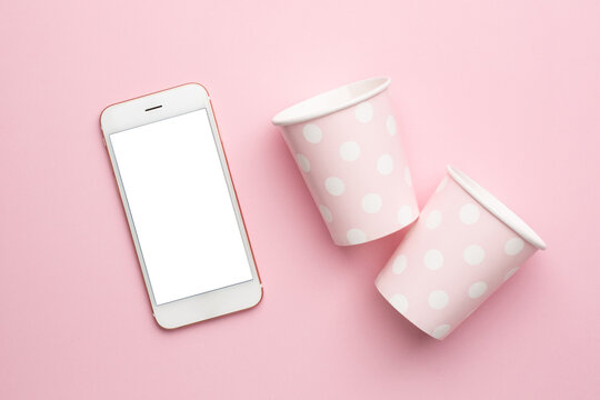 Mobile phone and polka dot disposable paper cups on pink background