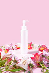 Obraz na płótnie Canvas Dispenser cosmetic bottle on pink background decorated with flowers. Presentation poster. Banner with place for text. Space for text. Mock up of cosmetic product. Shampoo, massage oil. Aromatherapy