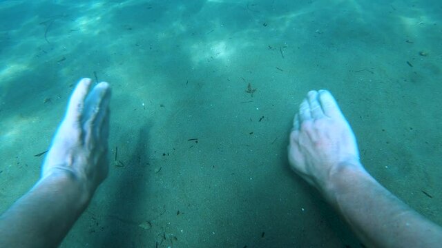 First person view diving in shallow sea water. Ocean floor seabed covered with fine sand. Male hands visible during diving. Concept of drowning and looking up to the surface. Slow motion, point of vie
