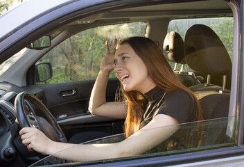 Naklejka premium Stressed young woman driver wth red hair is sitting inside her car and swearing at other drivers. Traffic jams concept. 