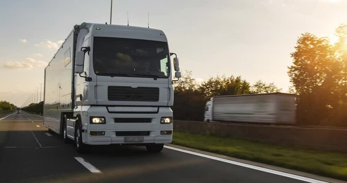 Cargo truck with cargo trailer driving on a highway. White Truck delivers goods in early hours of the Morning - very low angle drive thru close up shot.