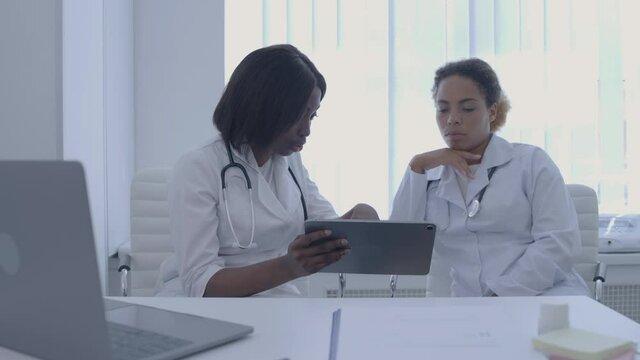 Qualified doctors discussing patient's test results, holding tablet, cooperation