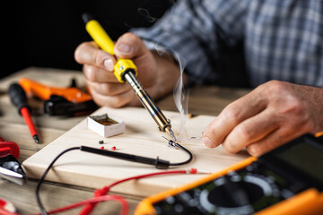 Electrician technician with electric soldering iron repairs the multimeter. People at work. Technology.