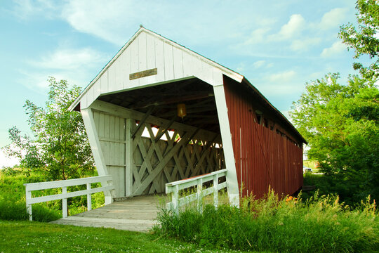 The Imes Covered bridge leaning to the left in Madison County, Iowa, three quarter view with trusses, cross beams, white railing, green trees, blue skies and white clouds Royalty free stock photo