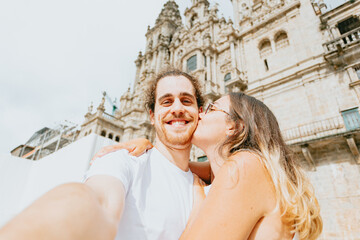 Horizontal shot of a young couple kissing in front of a cathedral during a sunny day