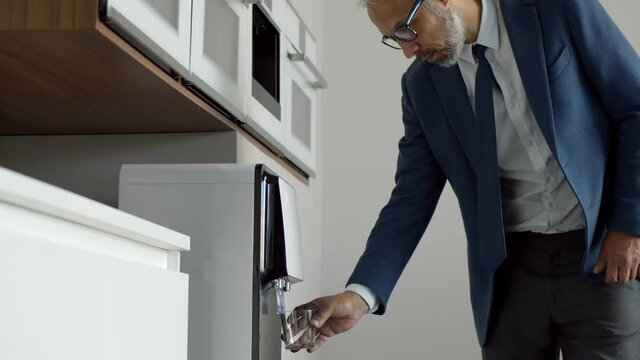 Mature businessman getting water from water cooler in modern office kitchen