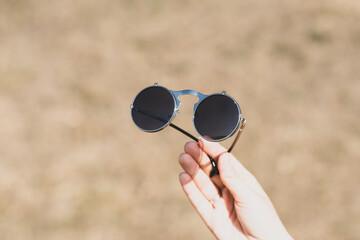 Fototapeta premium Steampunk sunglasses held in hand with round lenses retro flip up model close up shoot in a summer day. Selective focus