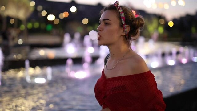 Funny woman blow the bubble with bubblegum near night fountain