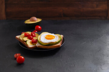 Healthy brekfast toasts with avocado, egg and tomatoes on the black stone background flat lay mock-up with copy space