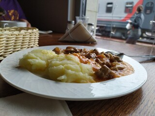White plate with mashed potatoes and meat goulash on the table in the cafe by the window