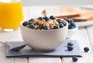 Breakfast with granola and blueberry, milk with orange juice and baked toasts on the white wooden table close-up