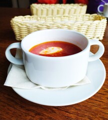 A white ceramic bowl of borscht and a bread basket on a brown wooden table